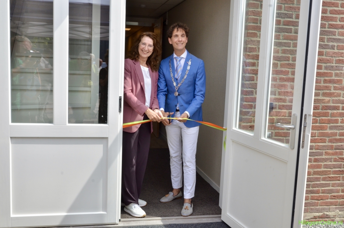 Twee personen staan in een deuropening en knippen gezamenlijk een lint door tijdens een officiële opening