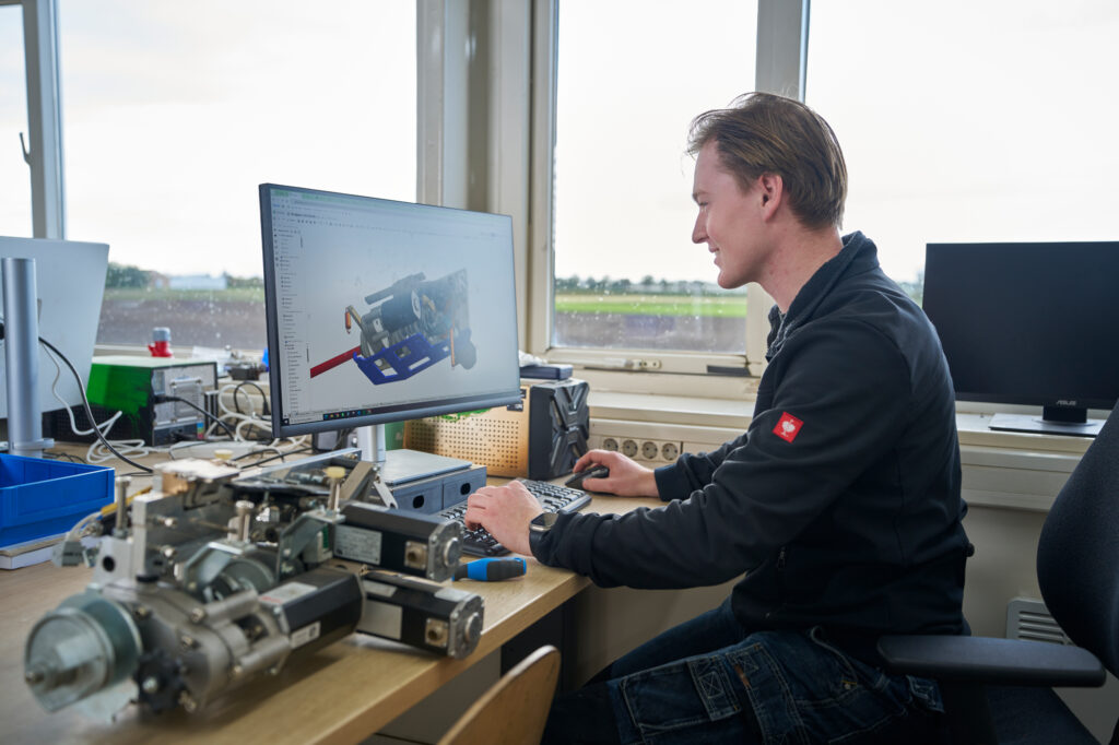 Medewerker van Ruigrok Groep werkt op kantoor aan een technische 3D-ontwerptekening op zijn computer, met onderdelen en elektronica op het bureau