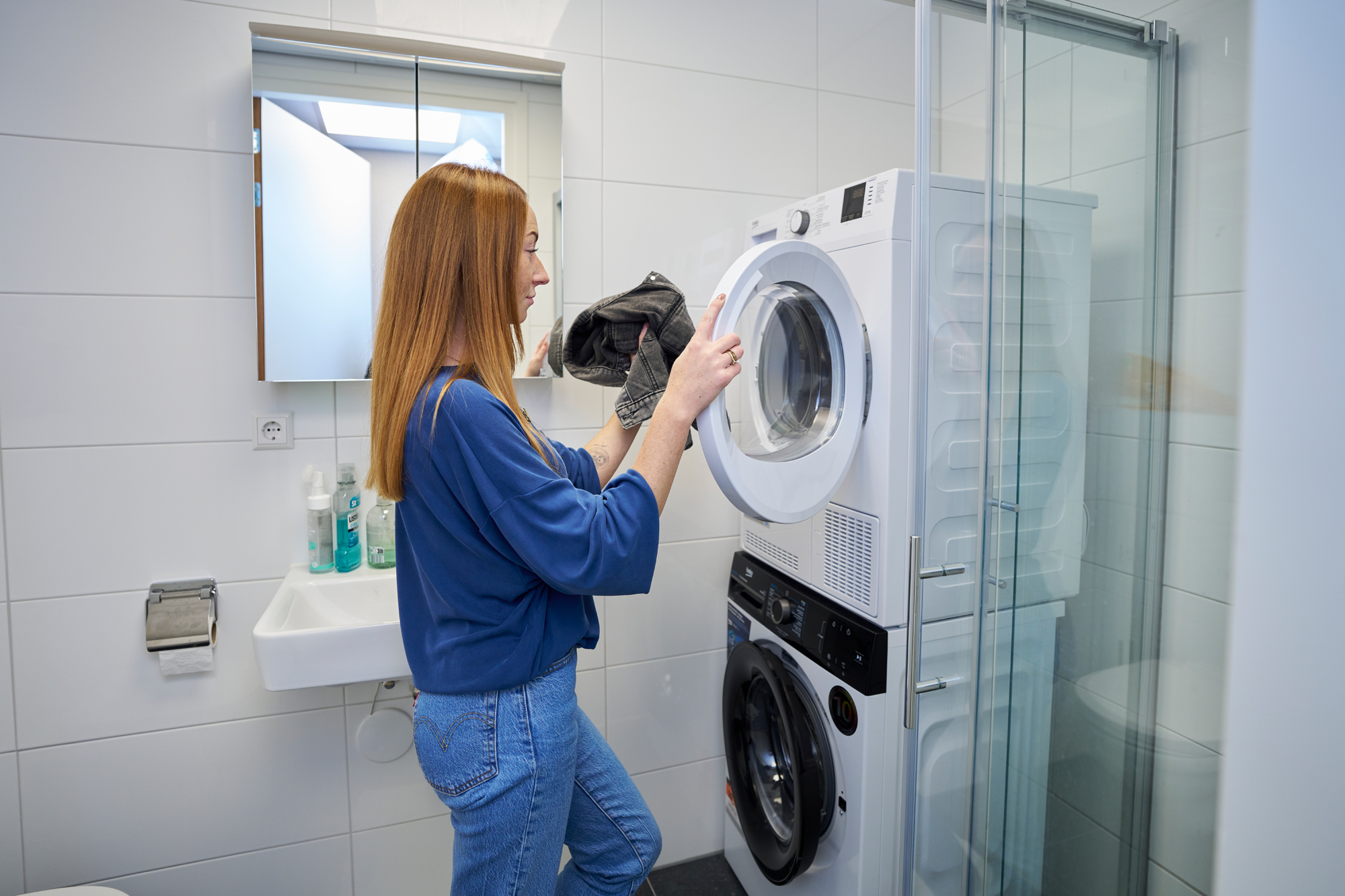 Vrouw doet de was in de badkamer van een woning van Ruigrok Groep, met een moderne wasmachine en droger naast de douchecabine